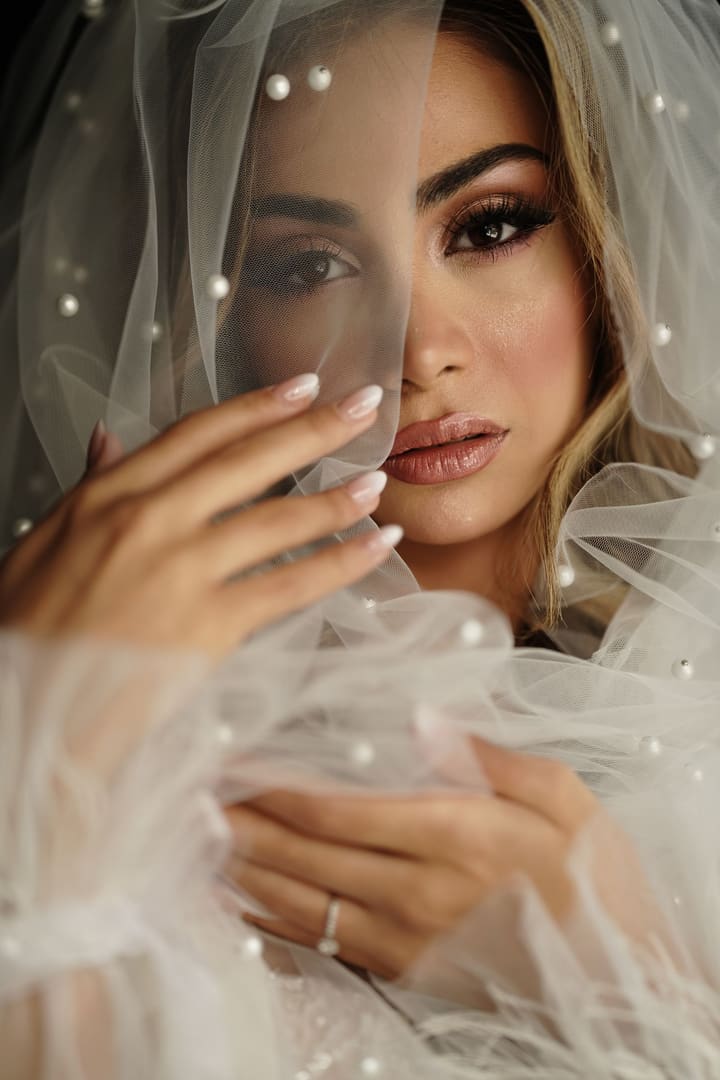 Bride half hidden behind a pearl-dotted veil, with a nude manicure