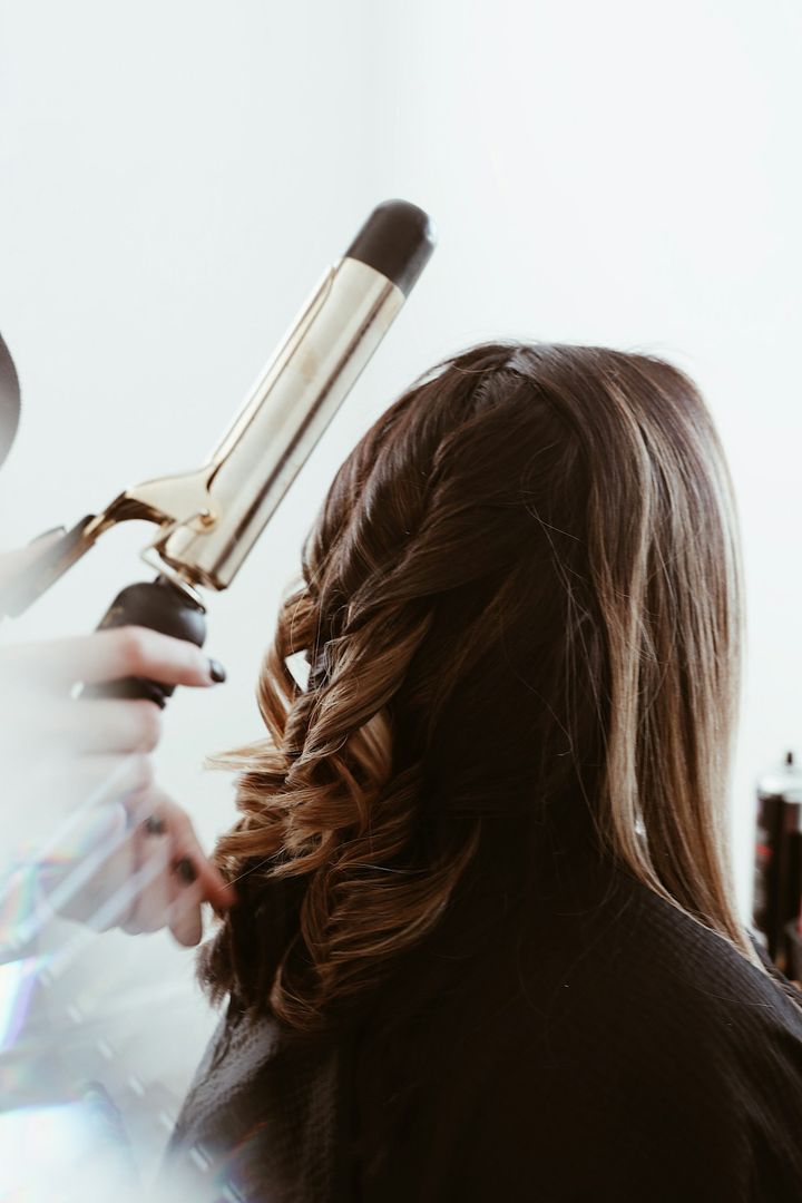 Stylist curling long brunette hair with a tong