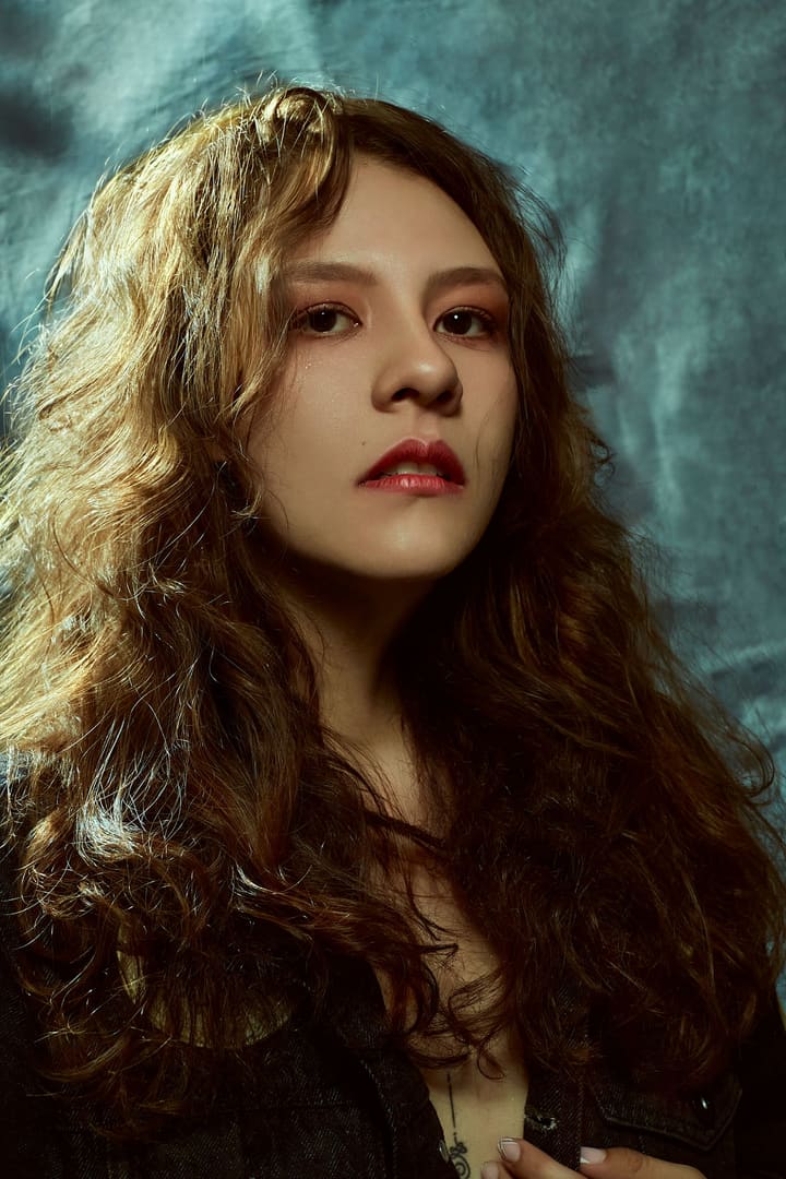 Deep red lip and long auburn curls against a teal backdrop