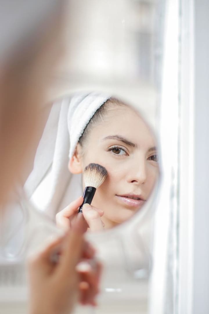 Powder being brushed onto a cheek, reflected in a round mirror