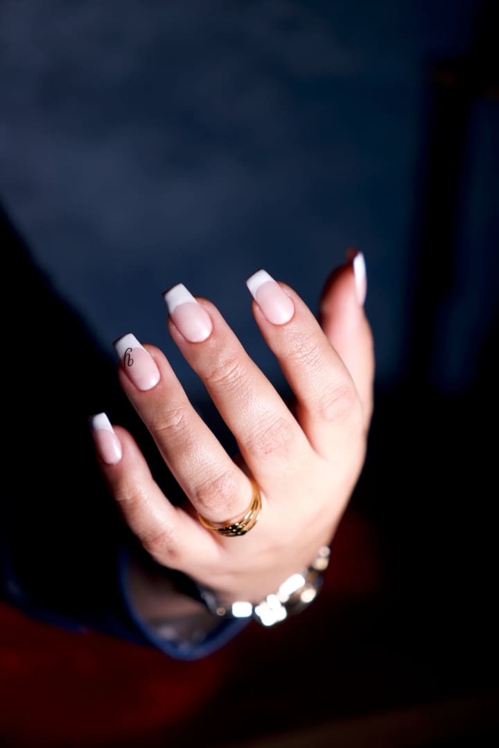 French-tip nails on a relaxed hand against a deep navy backdrop