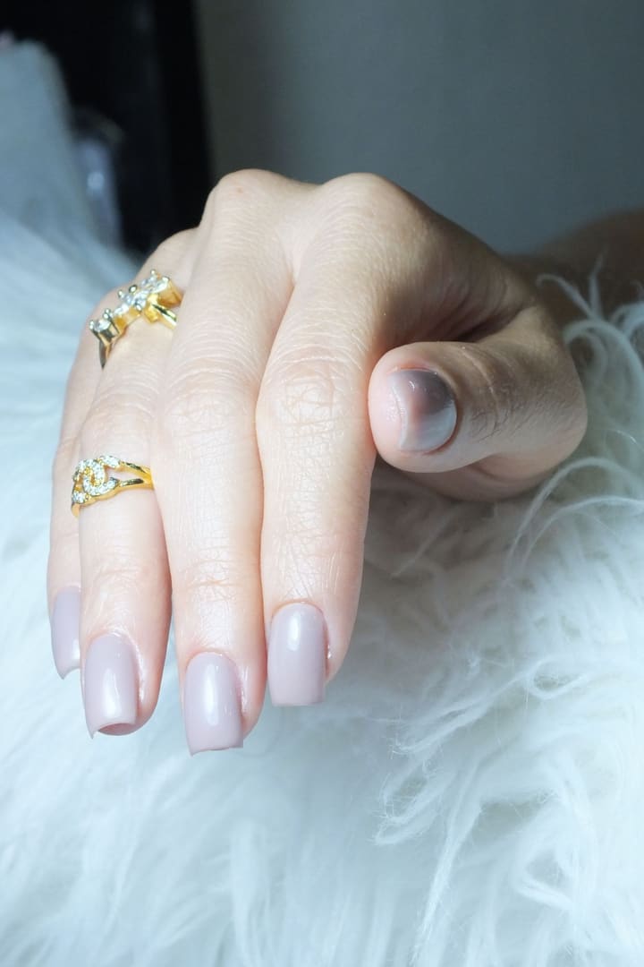 Pearl-pink square nails and gold rings resting on white feathers
