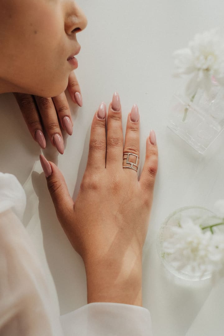 Blush almond nails resting on a white surface beside small white flowers