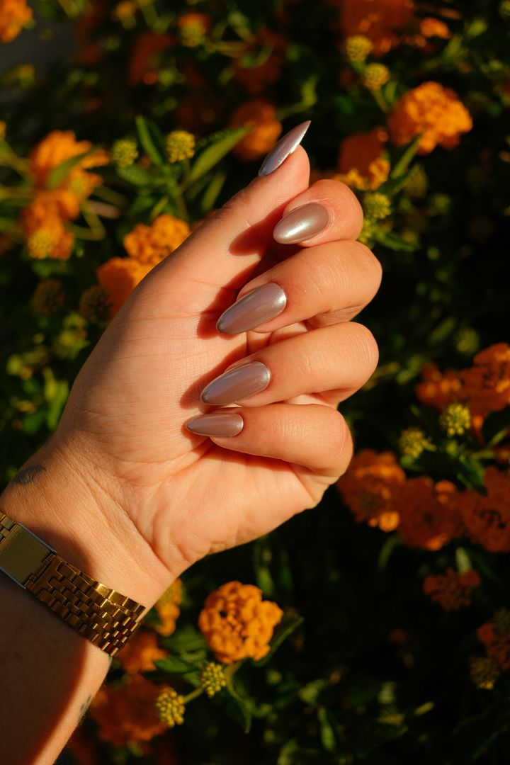 Glossy taupe almond nails and a gold watch among marigolds