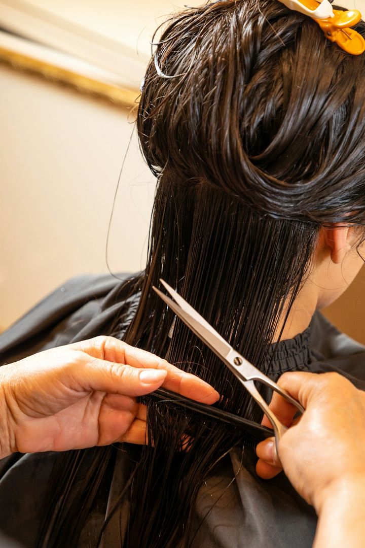 Stylist trimming wet dark hair with scissors and a comb