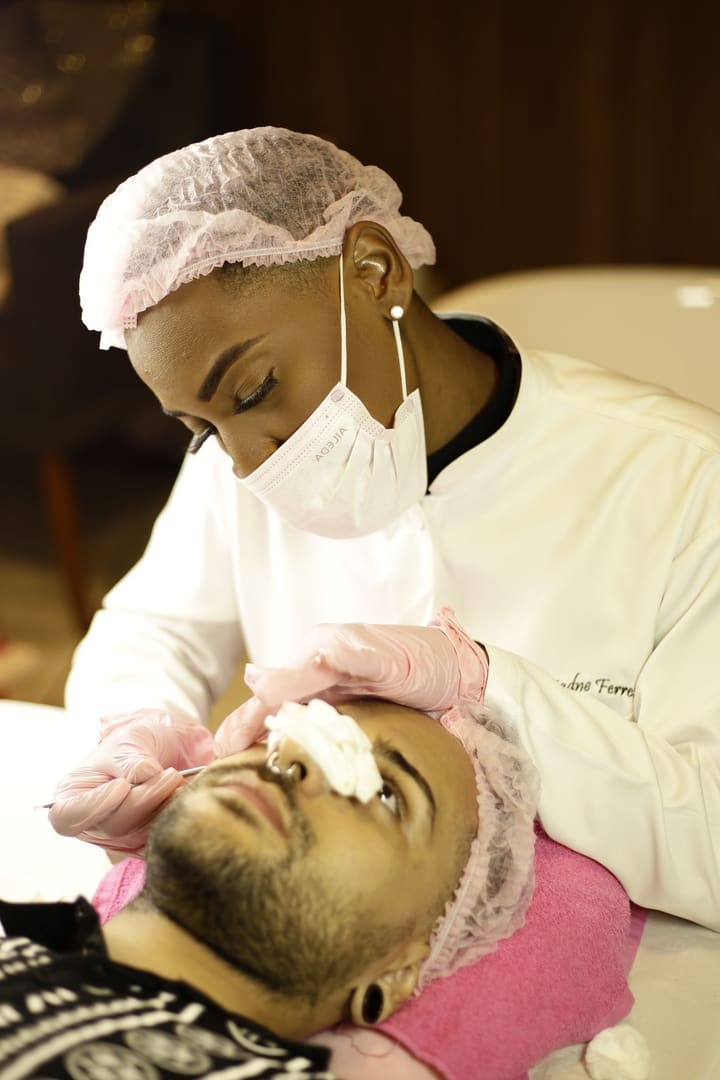 Aesthetician in a mask and cap cleansing a guest's face with cotton