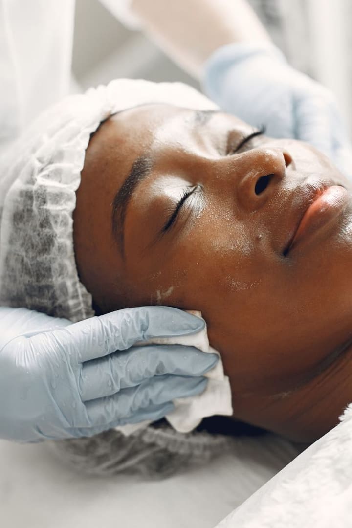 Gloved hands pressing a warm cloth to a guest's cheek during a facial