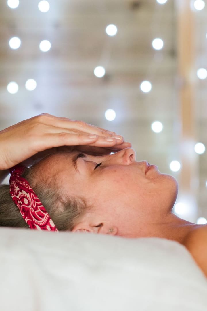 A hand resting on a guest's forehead in a softly lit treatment room