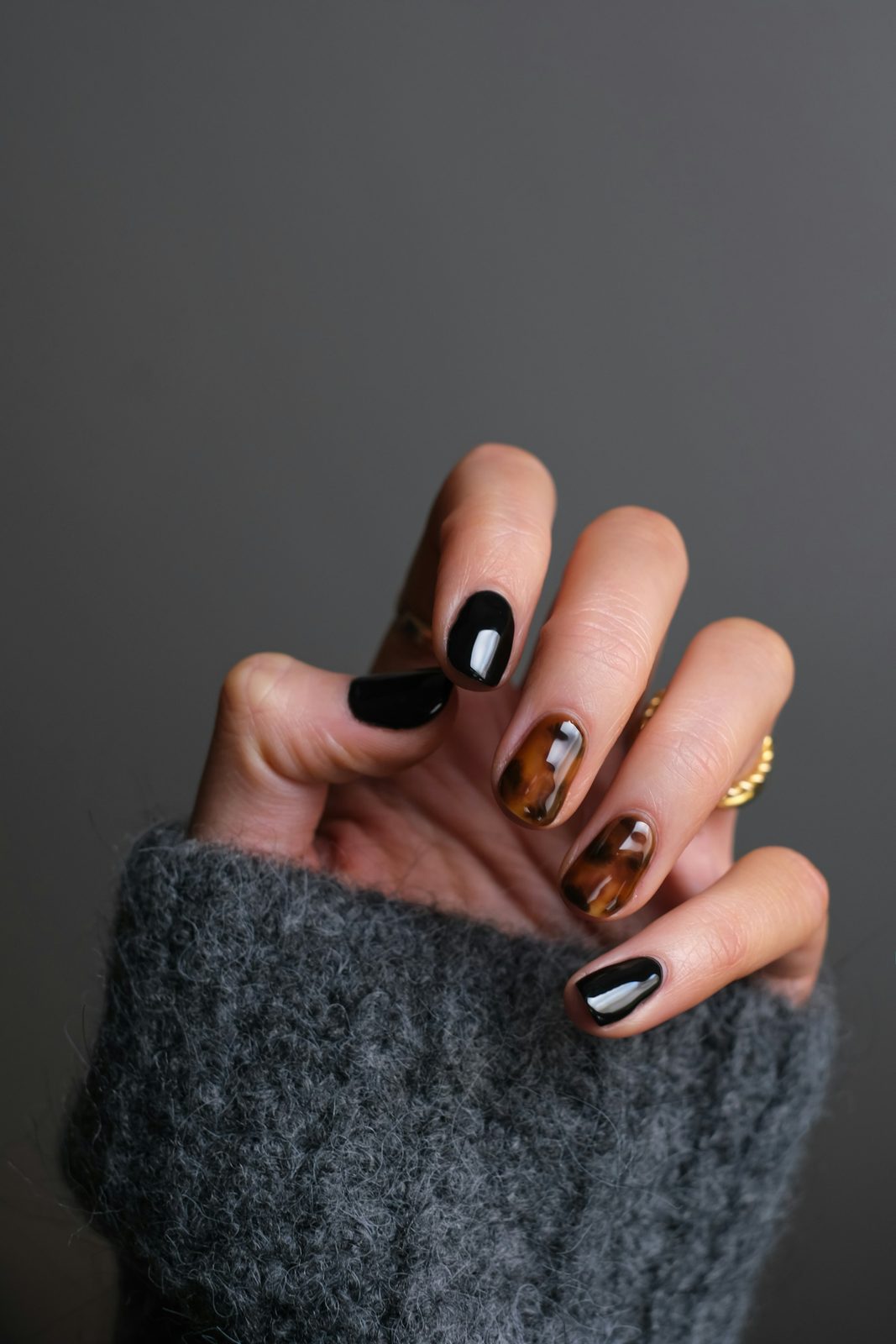 Black and tortoiseshell nails against a grey knit sleeve