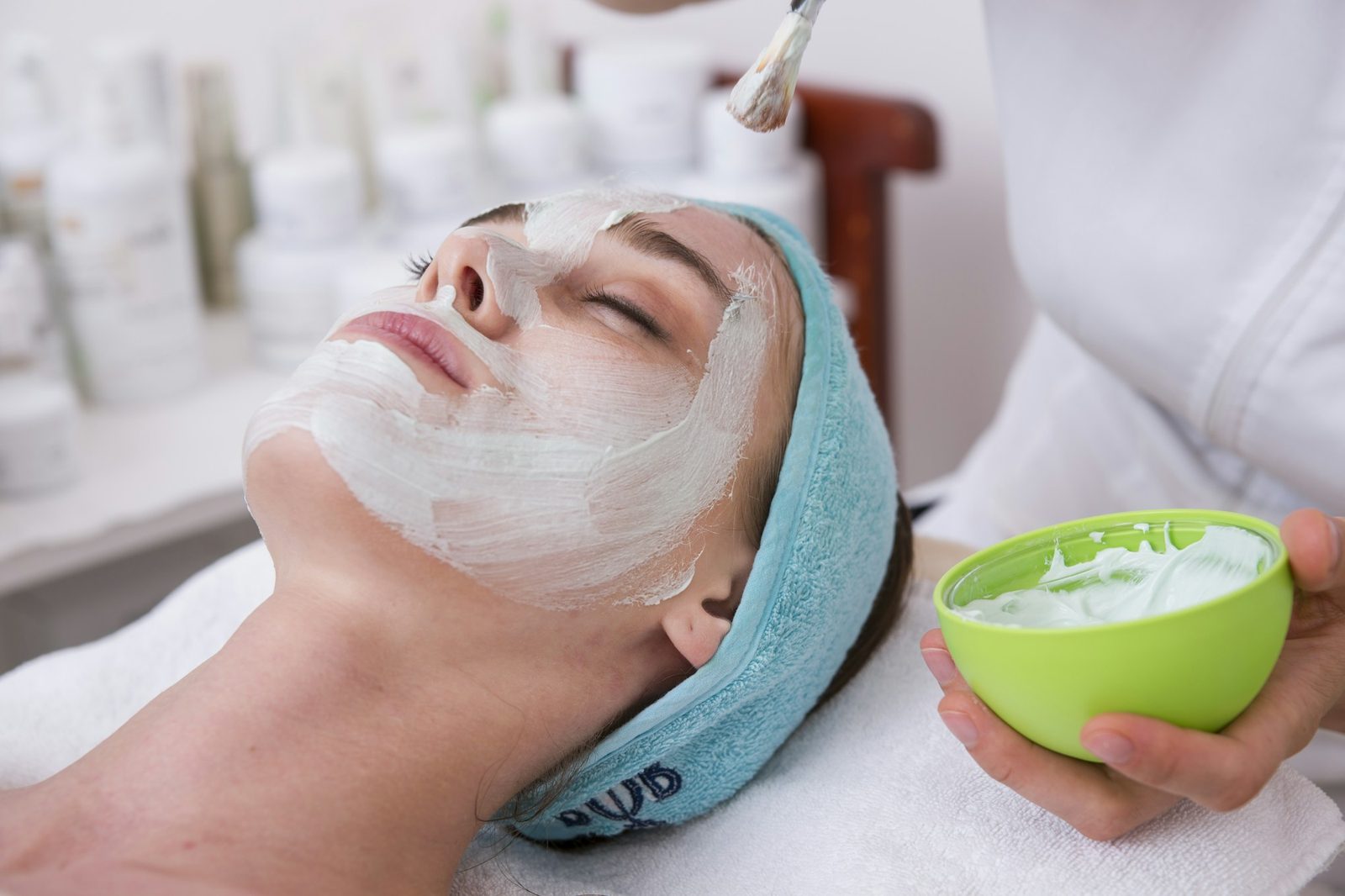 Aesthetician brushing a clay mask onto a guest wearing a blue headband