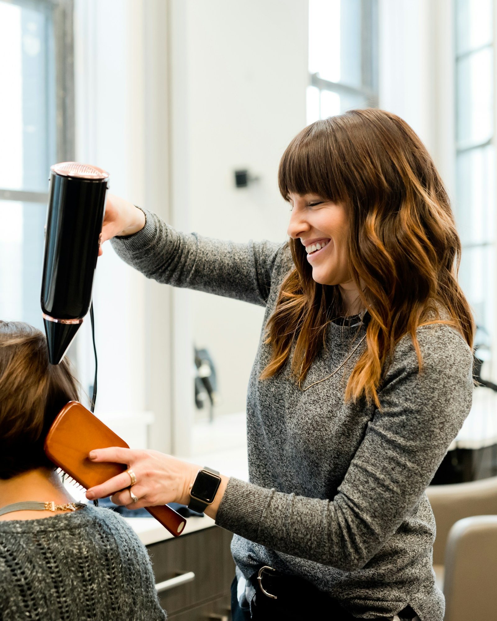 Stylist smiling as she blow-dries a client's hair in a bright, airy studio
