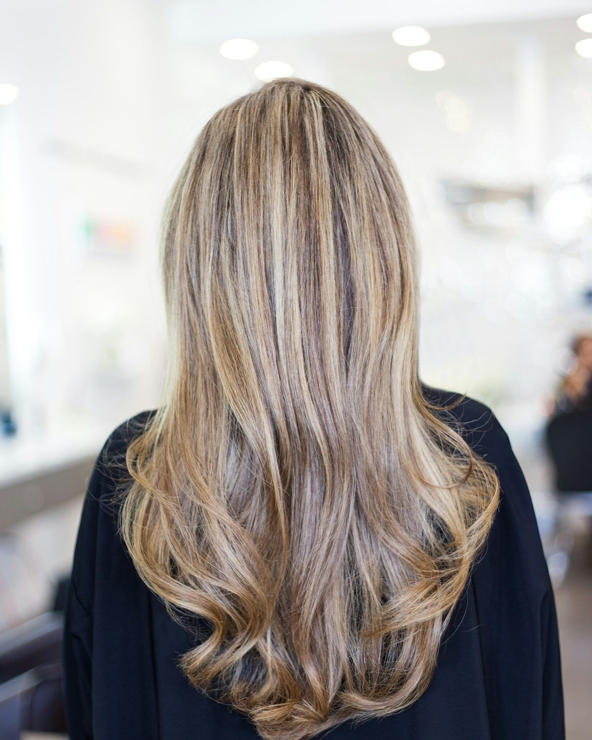 Back view of long, softly waved balayage hair in a bright salon