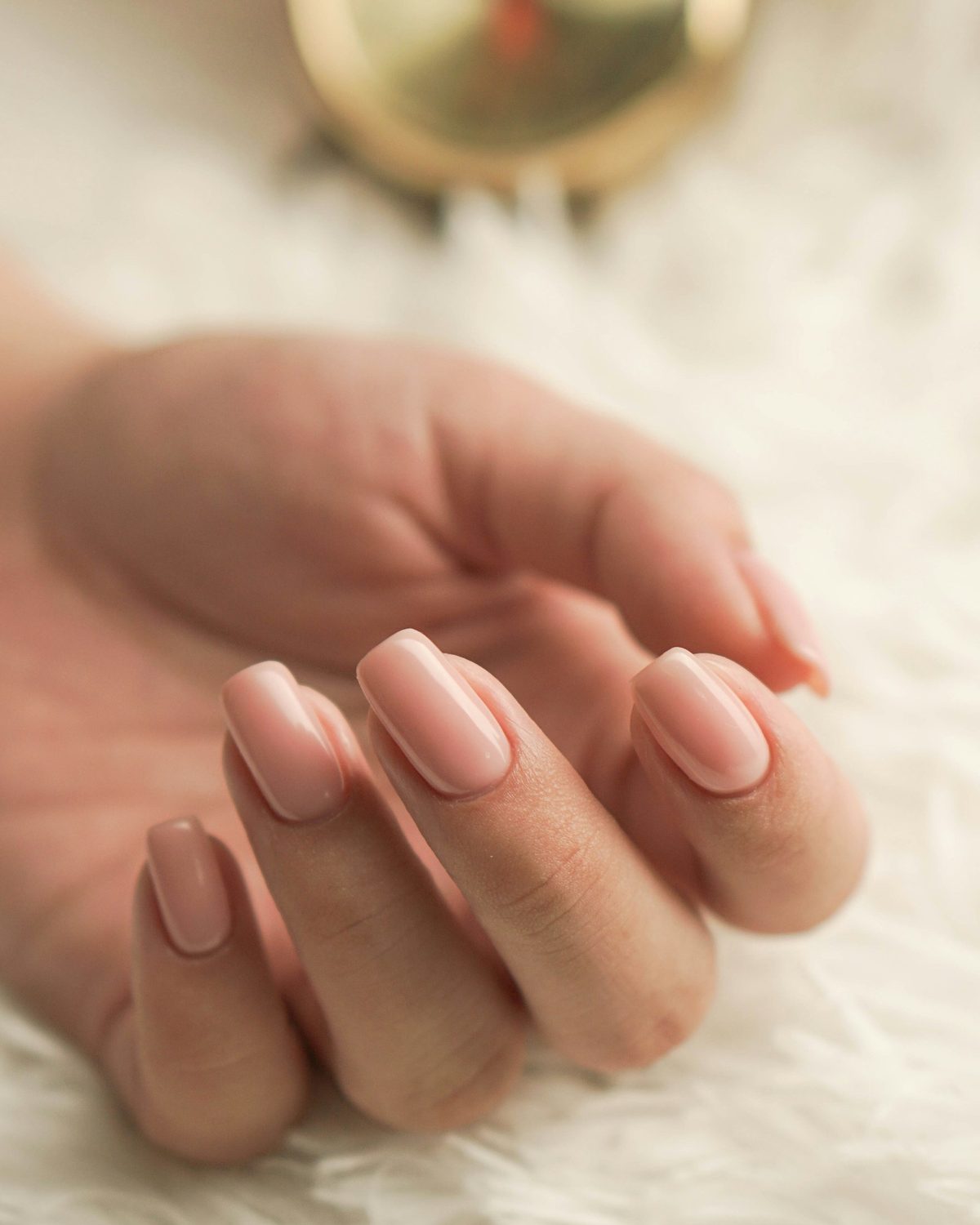 Hand with a glossy nude-pink manicure resting on soft white fur