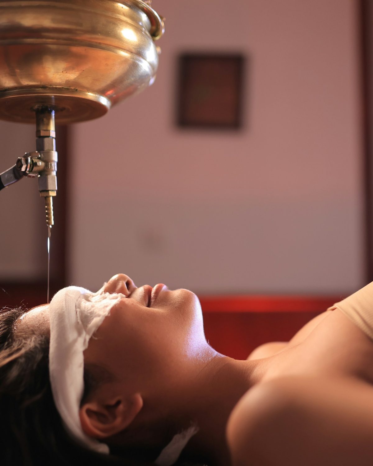 Guest resting beneath a brass vessel during an Ayurvedic shirodhara oil treatment